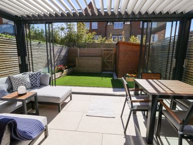 A sunroom with a sofa, a table, chairs, and a small garden with grass and a wooden shed at Captains Retreat Christchurch