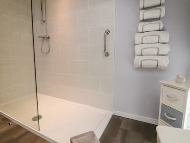 A shower area with tiled walls a glass panel and a towel rack with rolled white towels at Owls Nest in South Molton