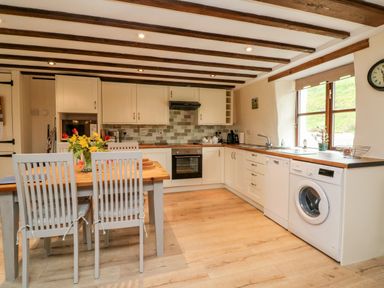 A kitchen with wooden table and chairs appliances and window at Owls Nest in South Molton