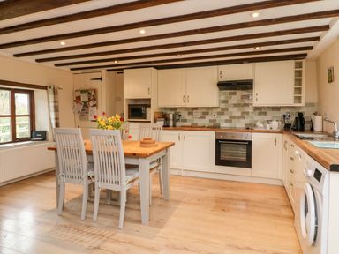 A kitchen with wooden beams a dining table with chairs and flowers on the table at Owls Nest in South Molton