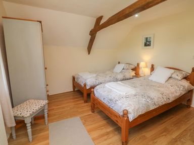 A bedroom with two single beds a wardrobe a bench and a lamp at Owls Nest in South Molton