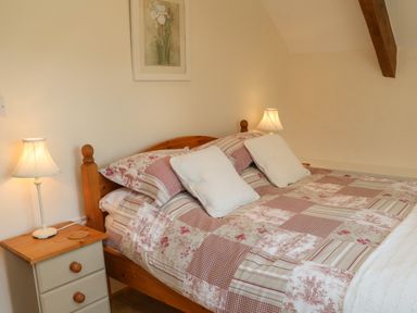 A bedroom with a wooden bed with a patterned bedspread two bedside tables with lamps and a floral picture on the wall at Owl's Nest in South Molton