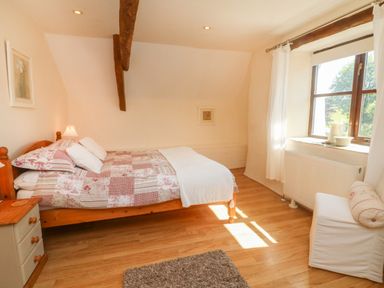 A bedroom with a wooden bed a nightstand a window with white curtains and a chair at Owls Nest in South Molton