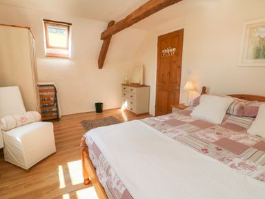 A bedroom with a wooden bed, a chest of drawers, a white chair, and a small window at Owl's Nest in South Molton