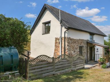 A stone and white plaster cottage with a front porch and wooden fence at Owl's Nest in South Molton