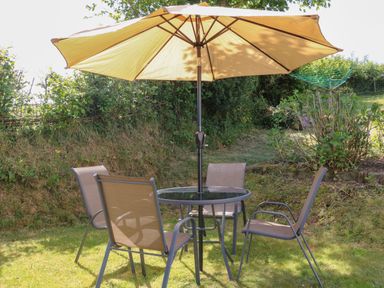 A garden with a round glass table and four chairs under a large beige umbrella at Owls Nest in South Molton