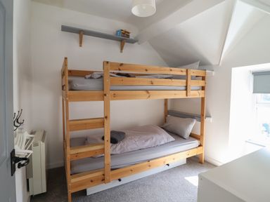 A small bedroom with wooden bunk beds a window with a roller blind and a wall shelf at Snowdon View in Harlech