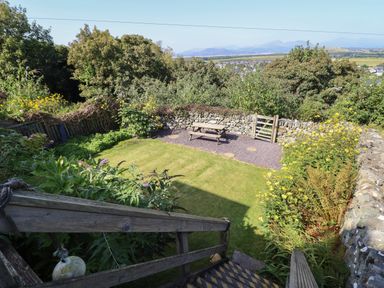A garden with grass and flowers surrounded by stone walls with a wooden picnic table and gate at Snowdon View in Harlech