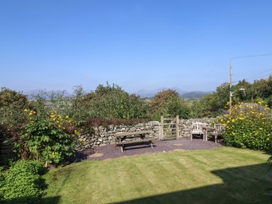 A garden with a stone wall picnic table wooden bench and yellow flowers at Snowdon View in Harlech