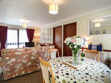 A living room with floral sofas a dining table with flowers on it and a sideboard with a mirror at Chy Lowenna Rosecraddoc Holiday Village near Liskeard