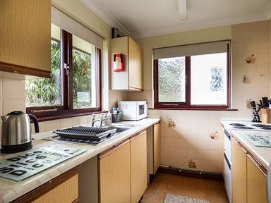 A kitchen with wooden cabinets a kettle dish rack microwave and stove at Chy Lowenna Rosecraddoc Holiday Village near Liskeard