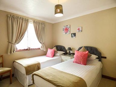 A bedroom with two single beds side by side with pink cushions and bedside table with lamp at Chy Lowenna Rosecraddoc Holiday Village near Liskeard