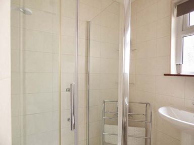 A bathroom with a glass shower enclosure a towel rack a wall-mounted sink and a window at Chy Lowenna Rosecraddoc Holiday Village near Liskeard