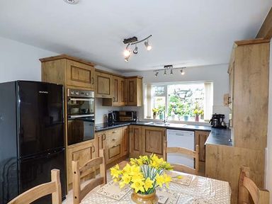 A kitchen with wooden cabinets black refrigerator and a table with yellow flowers at Simdda Wen Cottage in Llanddona near Beaumaris