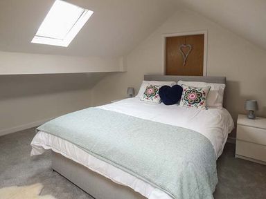 A bedroom with a bed with floral and heart shaped pillows a skylight and bedside tables with lamps at Simdda Wen Cottage in Llanddona near Beaumaris