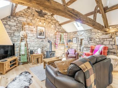 A living room with stone walls exposed wooden beams wood-burning stove and various seating at Berts Cottage Heights near Appleby-in-Westmorland
