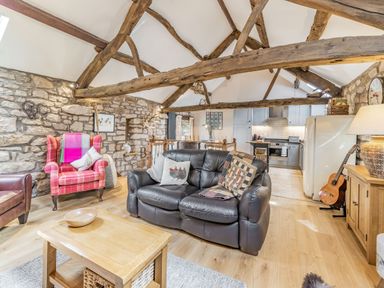 A living room with stone walls wooden beams a leather sofa armchairs a wooden coffee table and a kitchen area at Berts Cottage in Heights near Appleby-in-Westmorland