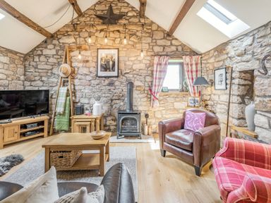 A living room with stone walls wooden beams a wood stove and leather and fabric chairs at Berts Cottage in Heights near Appleby-in-Westmorland