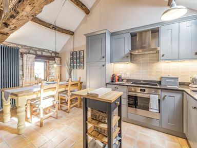 A kitchen with grey cabinets a wooden dining table and chairs and wooden beams at Berts Cottage in Heights near Appleby-in-Westmorland