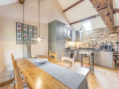 A kitchen and dining area with wooden table and chairs and stone wall at Berts Cottage Heights near Appleby-in-Westmorland