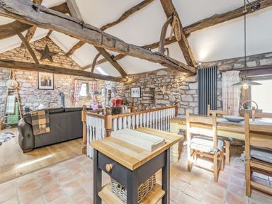 A combined dining and living area with wooden beams stone walls a dining table and chairs and a leather sofa at Berts Cottage Heights near Appleby-in-Westmorland