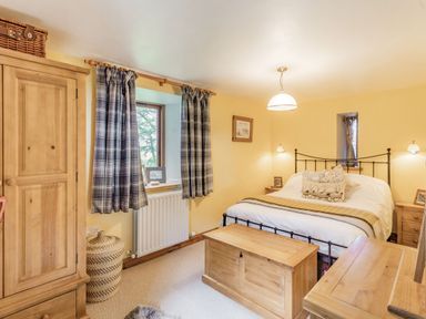 A bedroom with a double bed bedside tables a wooden chest a wardrobe and curtains at Berts Cottage Heights near Appleby-in-Westmorland
