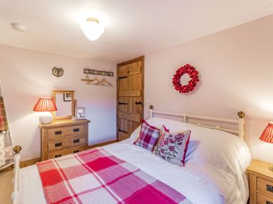 A bedroom with a bed covered in a red and white checkered blanket and pillows a wooden dresser with a mirror and a door on the wall at Berts Cottage Heights near Appleby-in-Westmorland