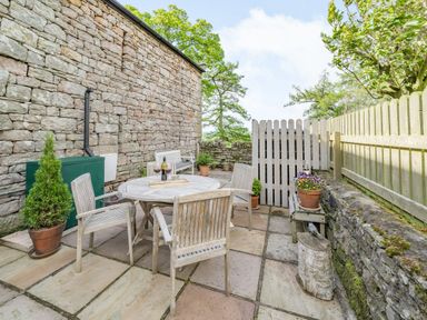 A stone patio with wooden table and chairs surrounded by stone walls and wooden fence at Berts Cottage Heights near Appleby-in-Westmorland