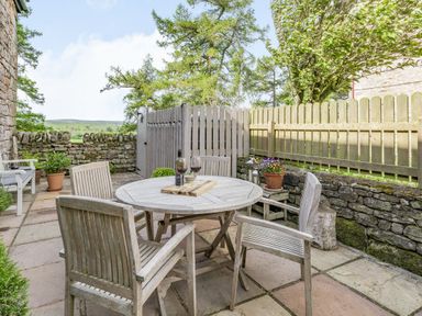 An outdoor patio with a round wooden table and four chairs with wine glasses and bottles at Berts Cottage Heights near Appleby-in-Westmorland