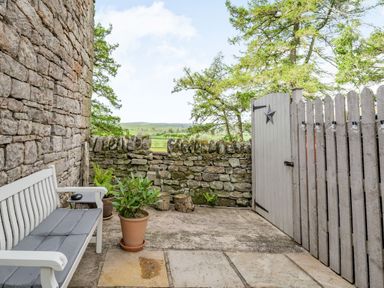 A stone wall outdoor patio with a bench potted plants wooden fence and gate at Berts Cottage Heights near Appleby-in-Westmorland