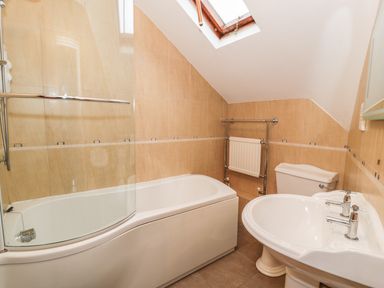 A bathroom with a bathtub and shower, toilet, sink, and skylight at Is Y Deri in Harlech
