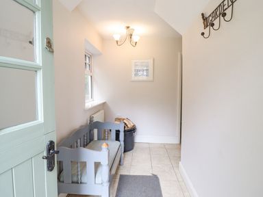 A small entryway with a wooden bench a window firewood in a black container and a garden sign on the wall at Is Y Deri in Harlech
