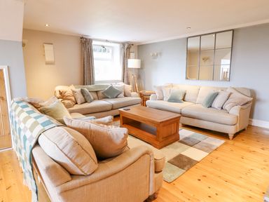 A living room with beige sofas a wooden coffee table a floor lamp and a large wall mirror at Is Y Deri in Harlech