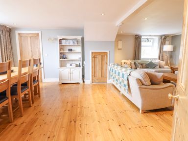 A living room with wooden floor a dining table with chairs a cabinet and sofas at Is Y Deri in Harlech