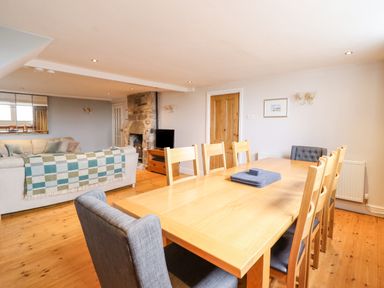 A dining area with a wooden table and chairs next to a living room with a sofa and fireplace at Is Y Deri in Harlech