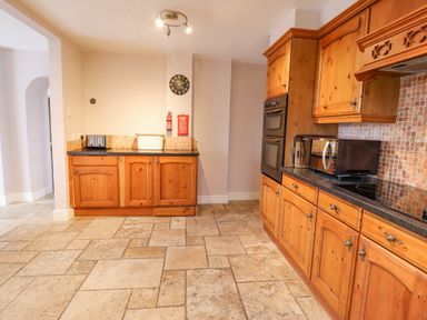 A kitchen with wooden cabinets a double oven a microwave a toaster and tiled flooring at Is Y Deri in Harlech