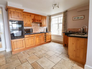 A kitchen with wooden cabinets black countertops a window and tiled floor at Is Y Deri in Harlech