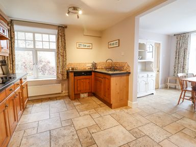 A kitchen with wooden cabinets a sink and a dining area with a table and chairs at Is Y Deri Harlech