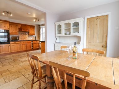 A dining area with a wooden table and chairs and a kitchen with wooden cabinets at Is Y Deri in Harlech