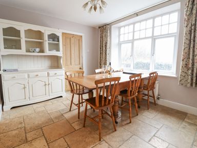 A dining room with wooden table and chairs a white cabinet and large window at Is Y Deri in Harlech