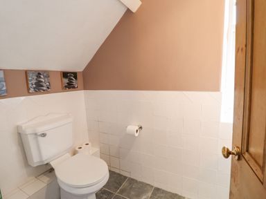 A bathroom with a toilet a toilet paper holder with roll and framed pictures above the toilet at Is Y Deri in Harlech