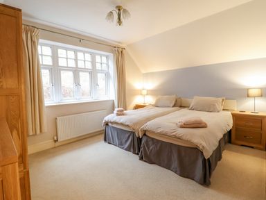 A bedroom with two single beds bedside tables with lamps a window and a wooden wardrobe at Is Y Deri in Harlech