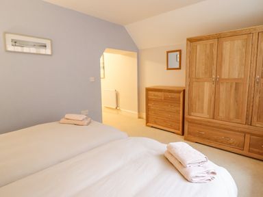 A bedroom with two single beds with folded towels a wooden dresser and wardrobe at Is Y Deri in Harlech