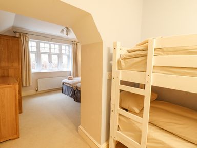 A bedroom with bunk beds on the right and twin beds near a window at Is Y Deri in Harlech