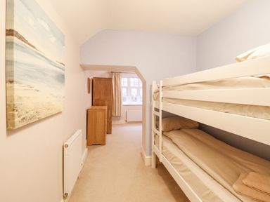 A bedroom with bunk beds a painting on the wall wooden cabinets and a window at Is Y Deri in Harlech
