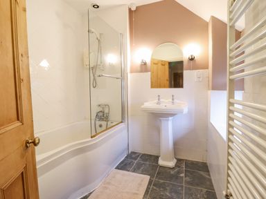 A bathroom with a bathtub shower combination a pedestal sink a wall mirror two wall lights a wooden door and a towel radiator at Is Y Deri in Harlech