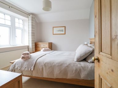 A bedroom with a wooden bed and chest of drawers and a window with curtains at Is Y Deri in Harlech