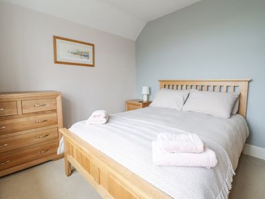 A bedroom with a wooden bed and dresser with towels on the bed at Is Y Deri in Harlech