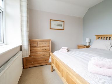 A bedroom with a wooden bed frame a wooden chest of drawers and a window with curtains at Is Y Deri in Harlech
