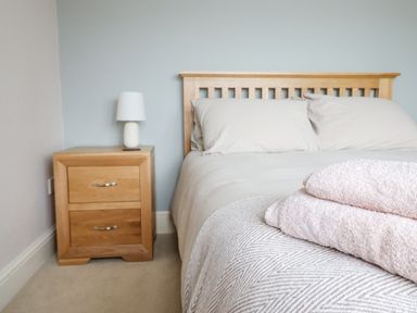 A bedroom with a wooden bed frame and bedside table with a lamp and folded towels at Is Y Deri in Harlech